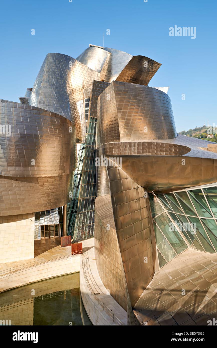 Besucher bewundern die einzigartige Struktur des Guggenheim Museums in Bilbao. Das Gebäude verfügt über moderne Architektur vor einem klaren blauen Himmel. Stockfoto