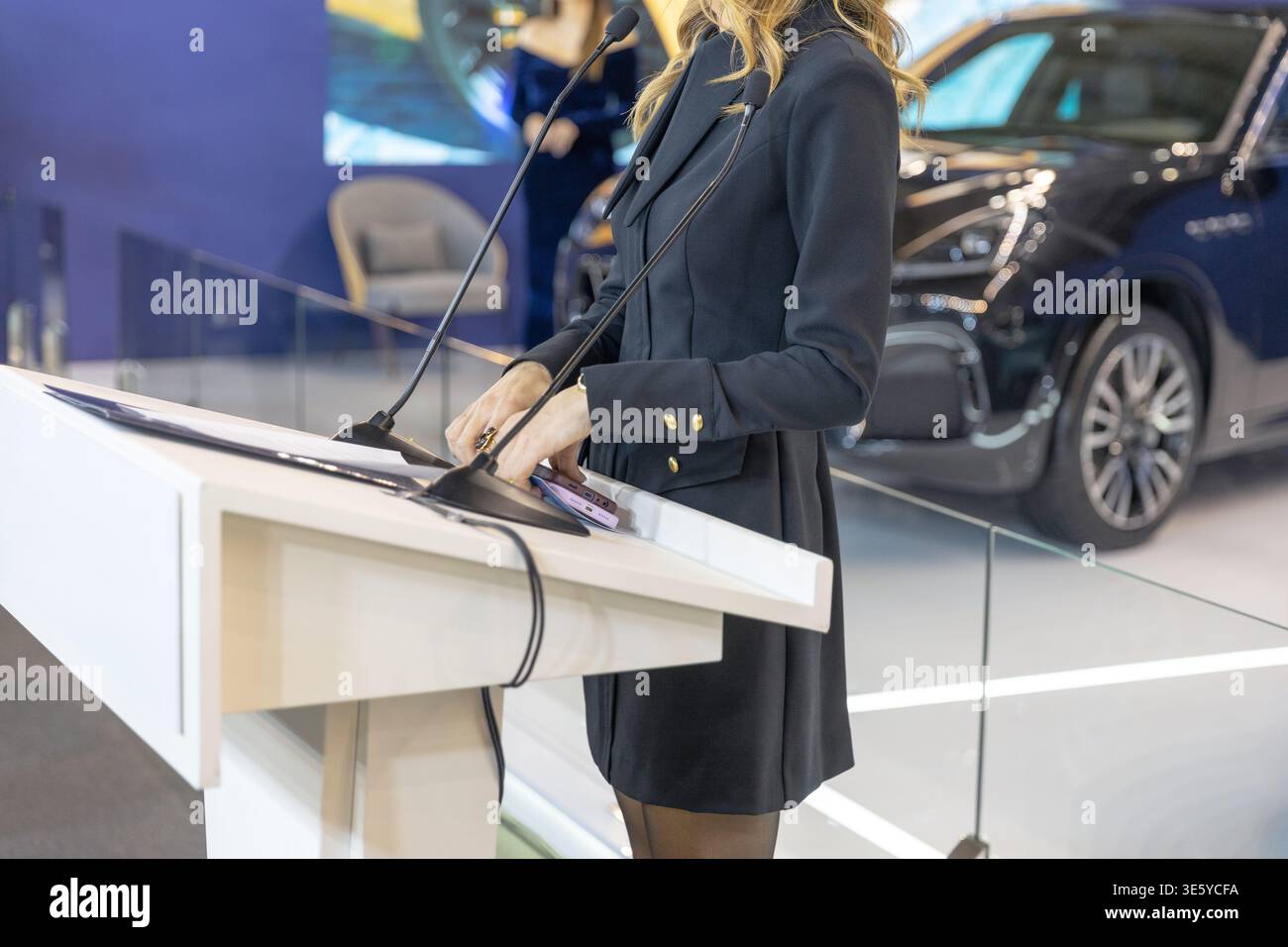 Selbstbewusste Geschäftsfrau, die auf dem Podium mit Mikrofonen spricht, bei der Präsentation von Autoausstellungen, in der Eventszene der Luxusautos Stockfoto