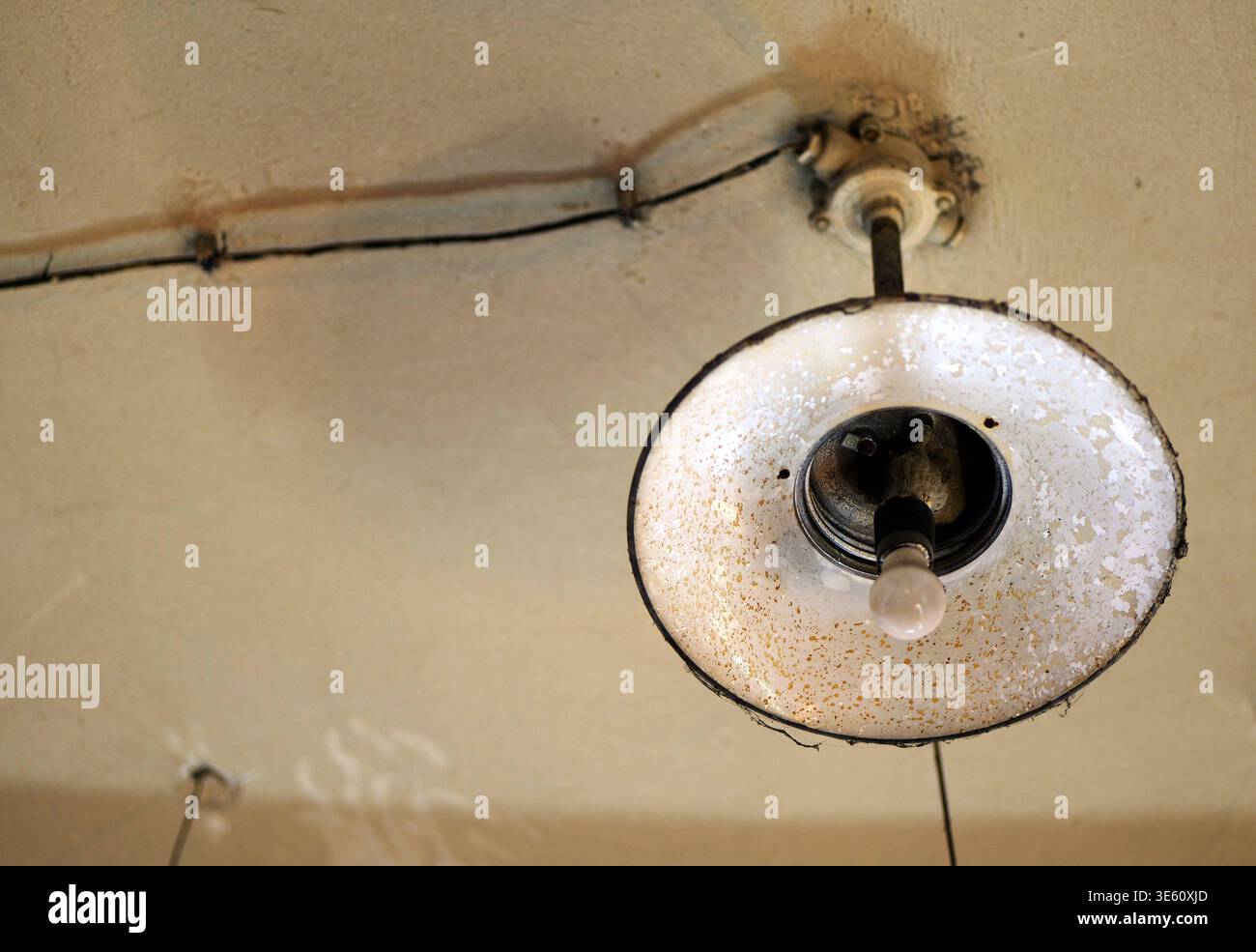 Nahaufnahme einer Vintage-Deckenleuchte aus Industrie mit emailliertem Metallschirm, freiliegender Verkabelung und warmer Glühlampe, die einen Retro-Fabrikstil einfängt Stockfoto