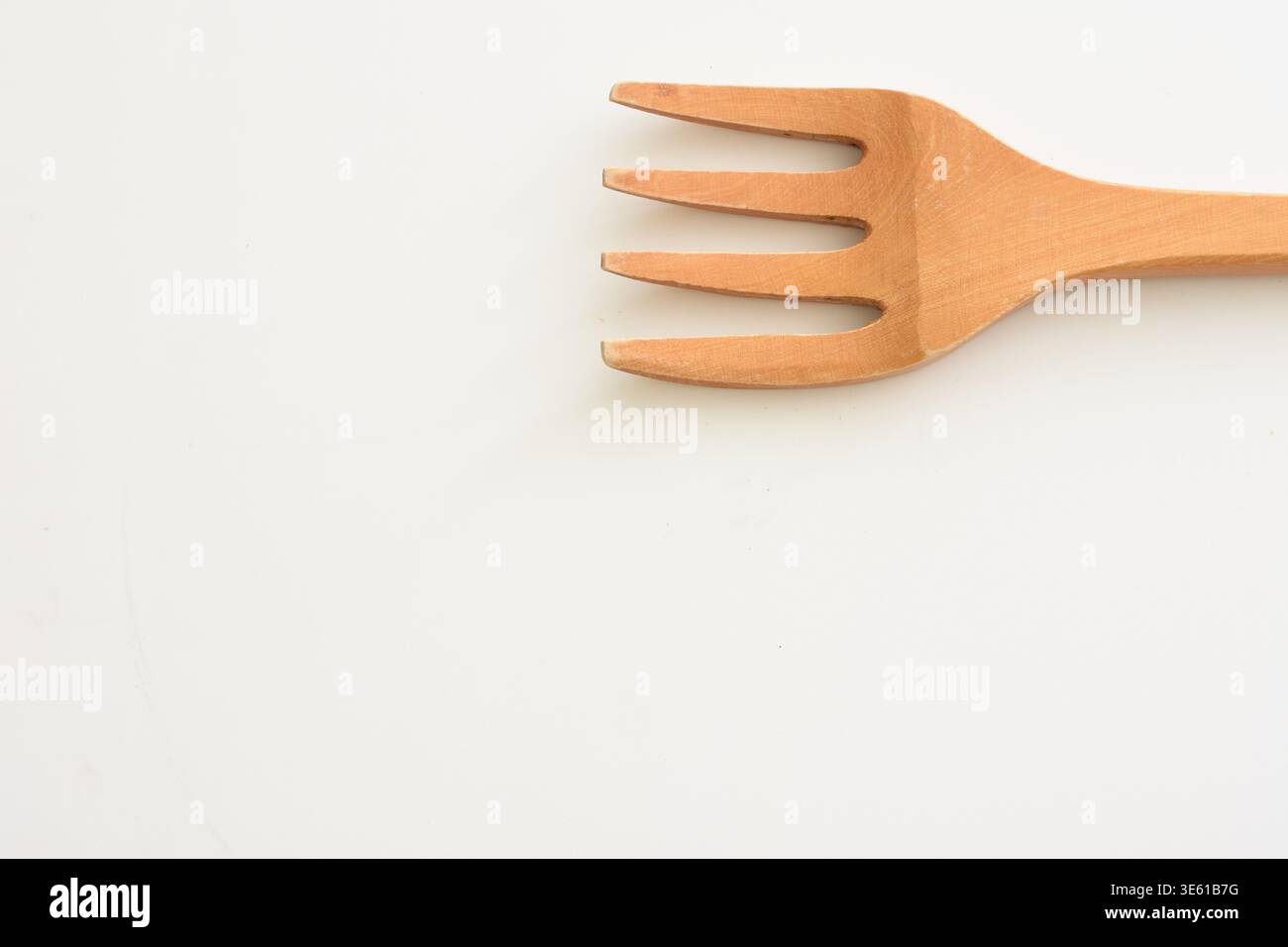 Einzelne Holzgabel auf einer weißen Oberfläche, die natürliche Textur und minimalistisches Design unterstreicht. Perfekt für Konzepte eines umweltfreundlichen Lebensstils Stockfoto