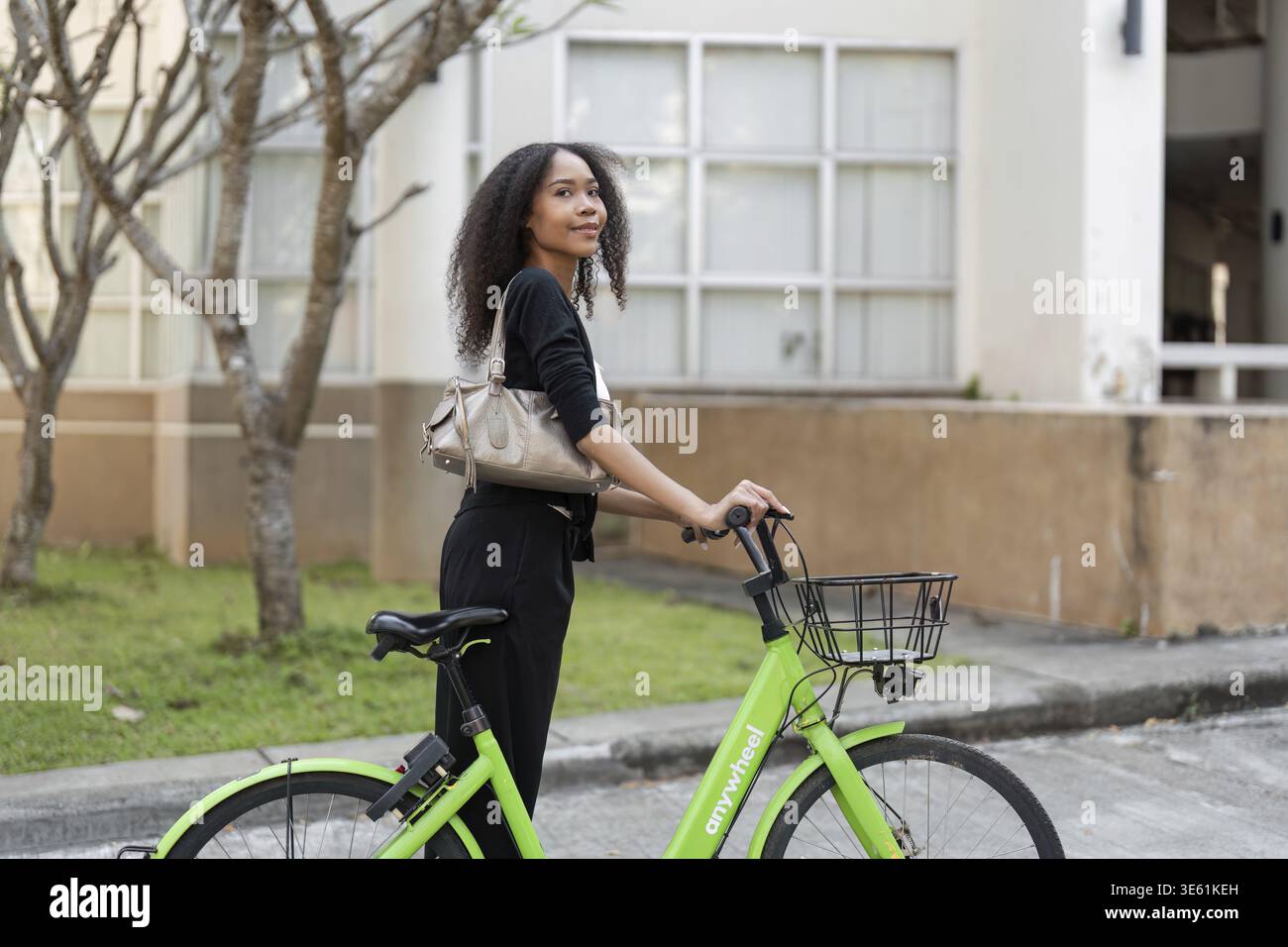 Eine selbstbewusste junge Frau posiert mit ihrem grünen Fahrrad, bereit, die Stadt zu erkunden und einen aktiven, umweltfreundlichen Lebensstil zu genießen Stockfoto