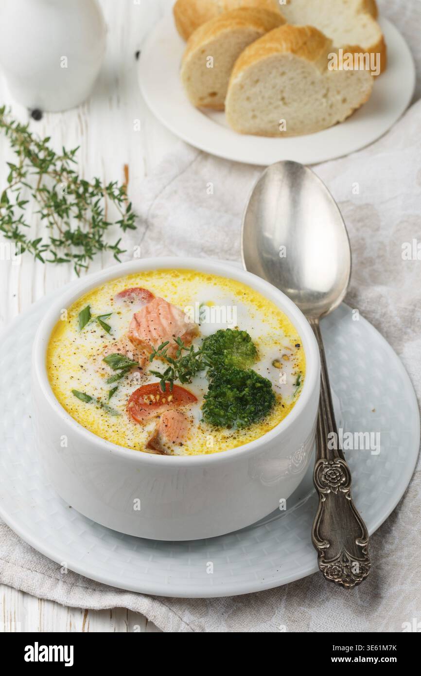 Lachs cremige Suppe mit Gemüse - Kartoffeln, Karotten, Tomaten und Brokkoli in einer weißen Schüssel auf hellem Holztisch Stockfoto