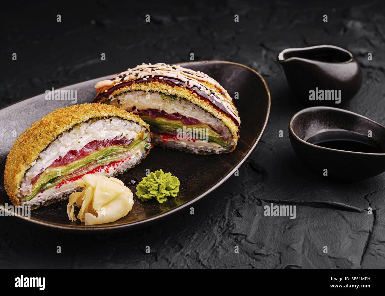 Speisen, Ein farbenfroher Sushi-Burger mit Schichten Sushi-Reis, Gemüse und Meeresfrüchten, serviert auf einem dunklen Teller. Begleitet von Garnituren und eintauchender Sau Stockfoto