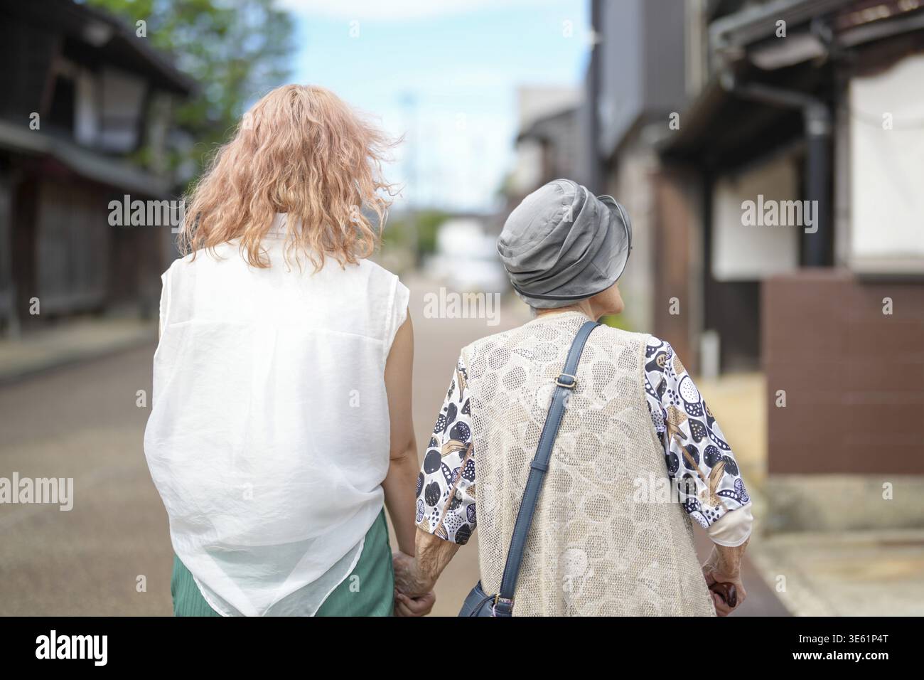 Zwei Frauen gehen die Straße entlang, eine trägt ein weißes Hemd. Die Frau im weißen Hemd hält die Hand der Frau in der grauen Weste Stockfoto