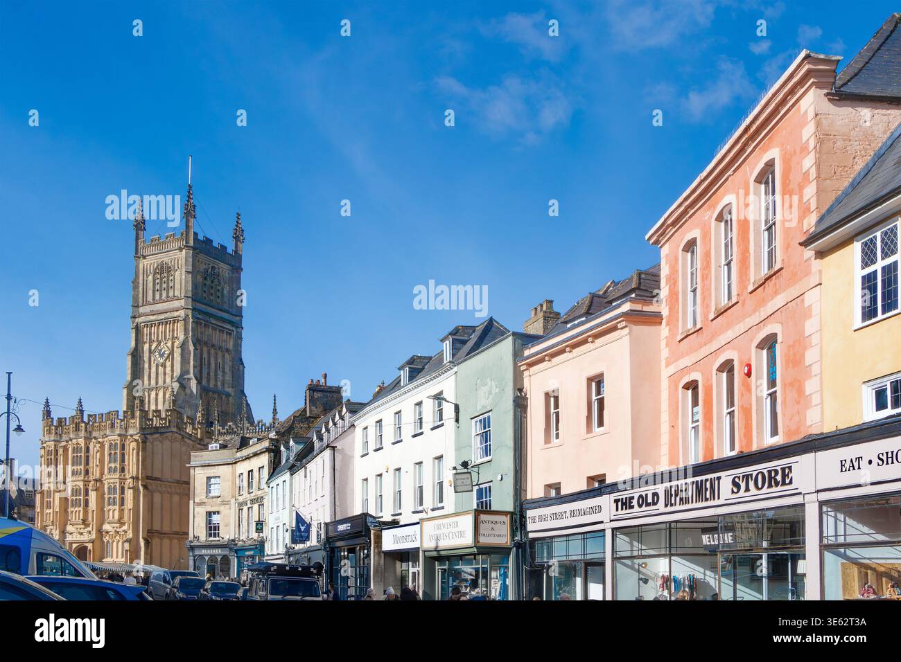 Historische Cirencester Parish Church of St John Baptist und traditionelle farbenfrohe Ladenfassaden am Marktplatz von Cirencester Gloucestershire England Stockfoto