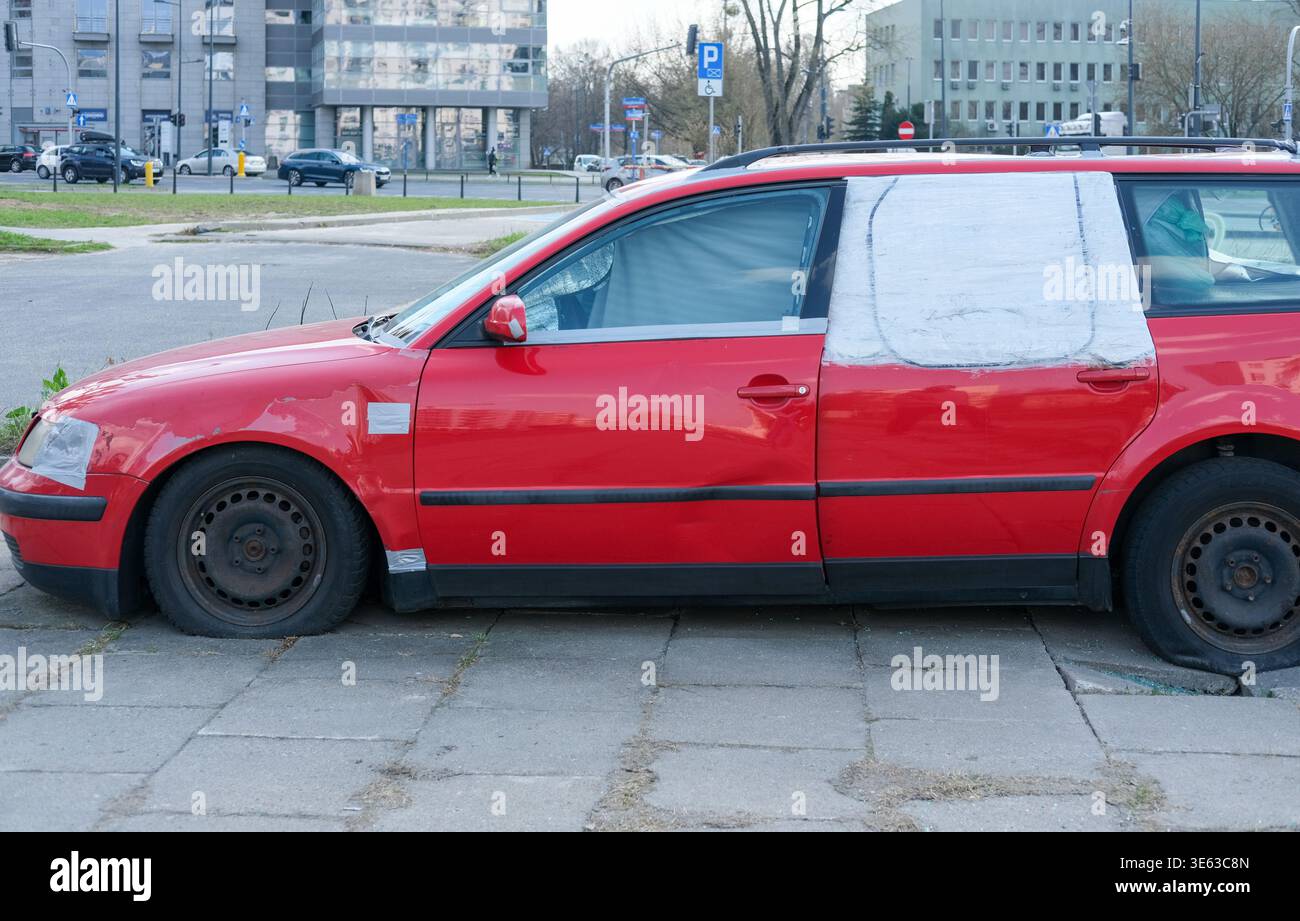 Roter Kombi mit verklebtem Fenster und sichtbaren Schäden parkt entlang einer Stadtstraße Stockfoto