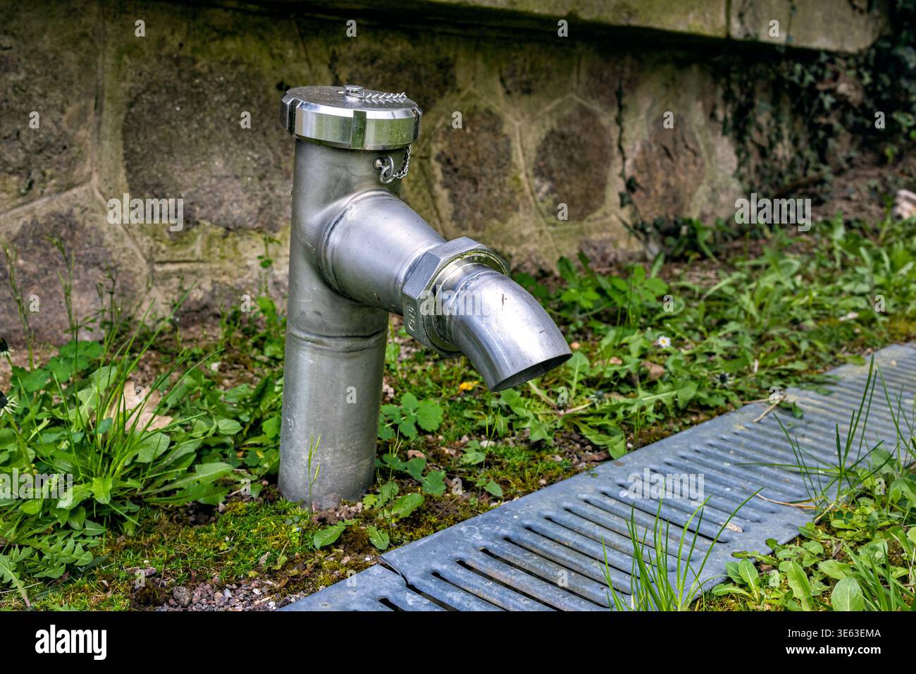 Ein L-förmiges Rohr oder Wasserhahn aus Edelstahl mit großem Durchmesser über einem Bodenabflusssystem. Industrielle Wasserwirtschaft mit einem verzinkten Metall Stockfoto