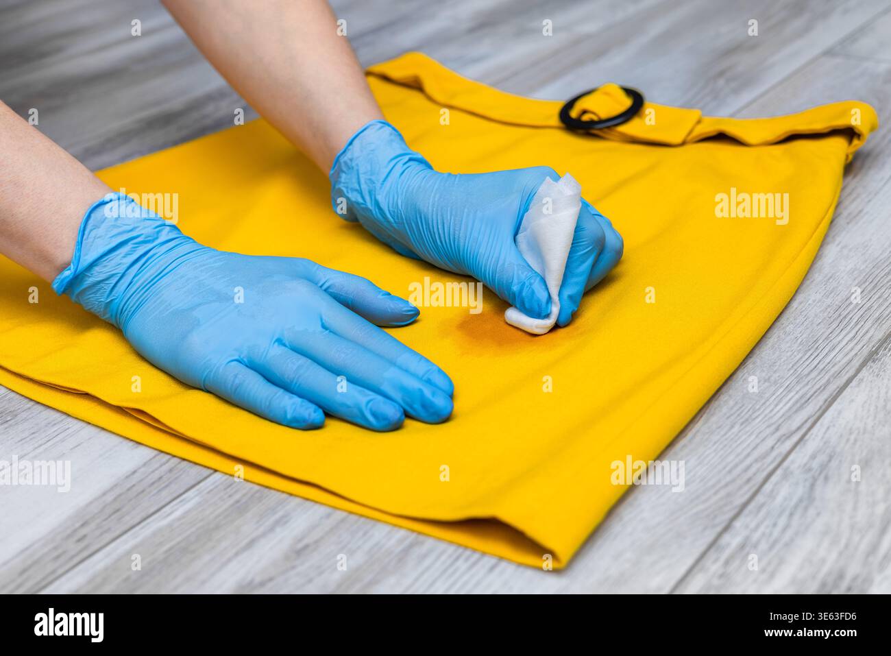 Die Hand einer Frau hält einen Fleckenentferner, um einen schmutzigen Fleck aus einem Rock zu entfernen. Stockfoto