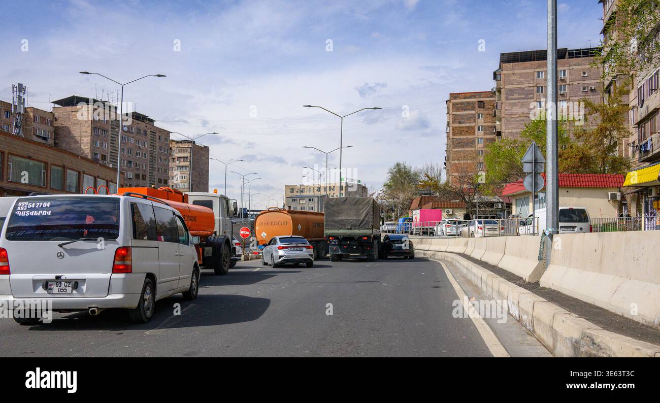 Urbane Straßenszene mit starkem Verkehr und Baufahrzeugen. Fahrzeuge fahren langsam durch Stadtstraßen bei klarem Himmel. Gebäude säumen beide Seiten mit Stockfoto