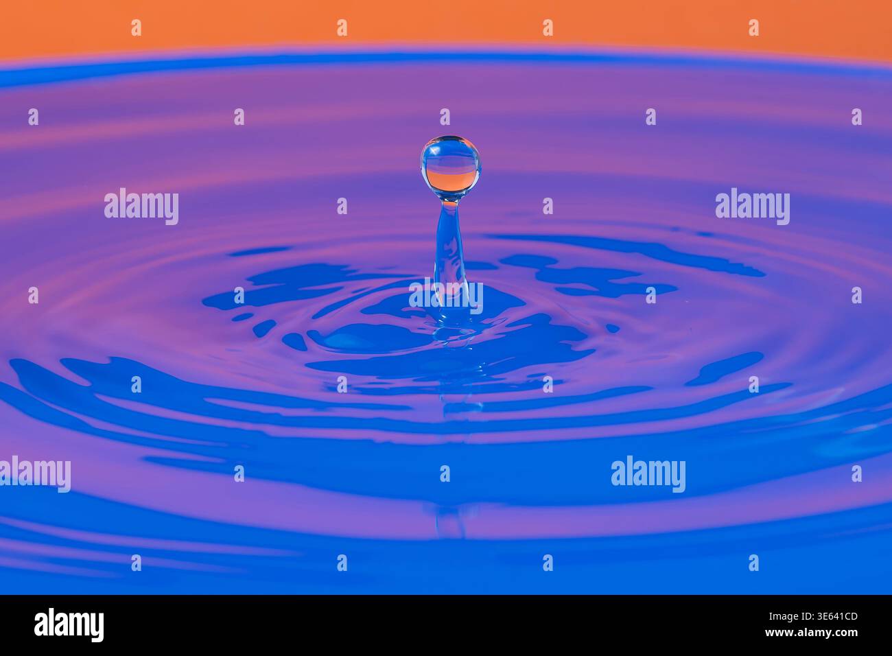 Ein Tropfen Wasser fällt und prallt in einem blau-orange gefärbten Gewässer Stockfoto