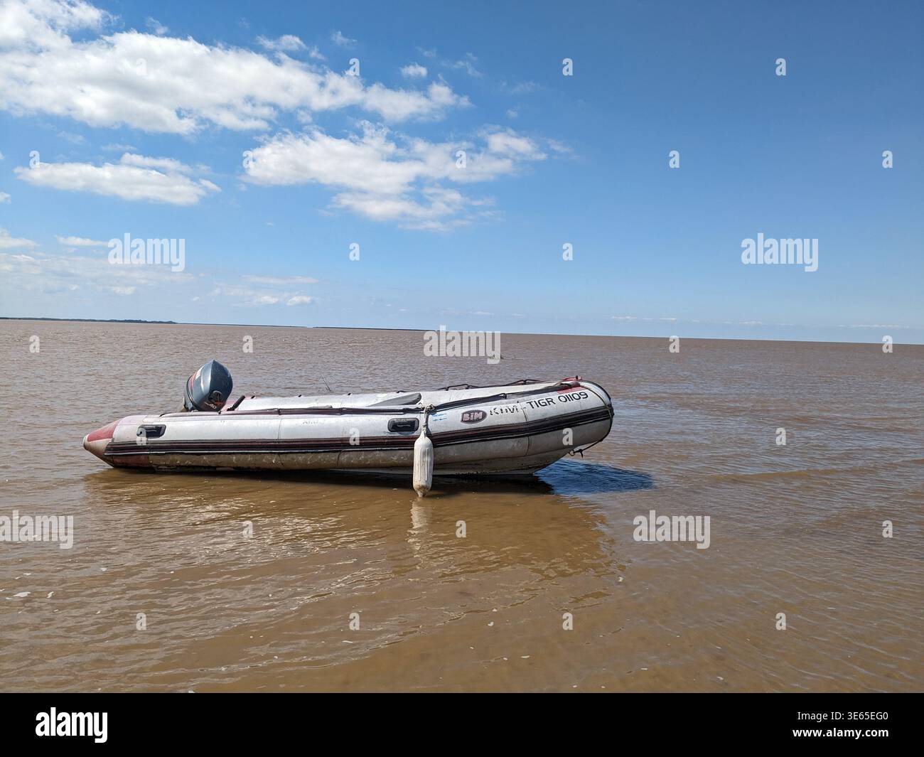 Nahaufnahme eines leeren starren Schlauchbootes (RIB) mit Außenbordmotor, das auf dem ruhigen, matschigen, braunen Wasser des Paraná-Deltas in Argentinien schwimmt. - Smartphone-aufgenommenes Stockfoto