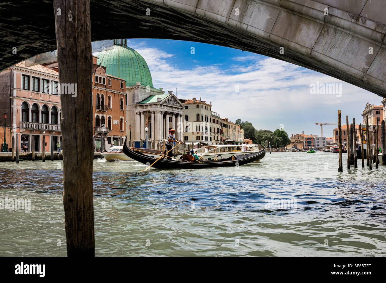Blick unter einer venezianischen Brücke mit Gondeln auf dem Kanal, eingerahmt von historischen Gebäuden und einer Kuppelkirche in der Ferne Stockfoto