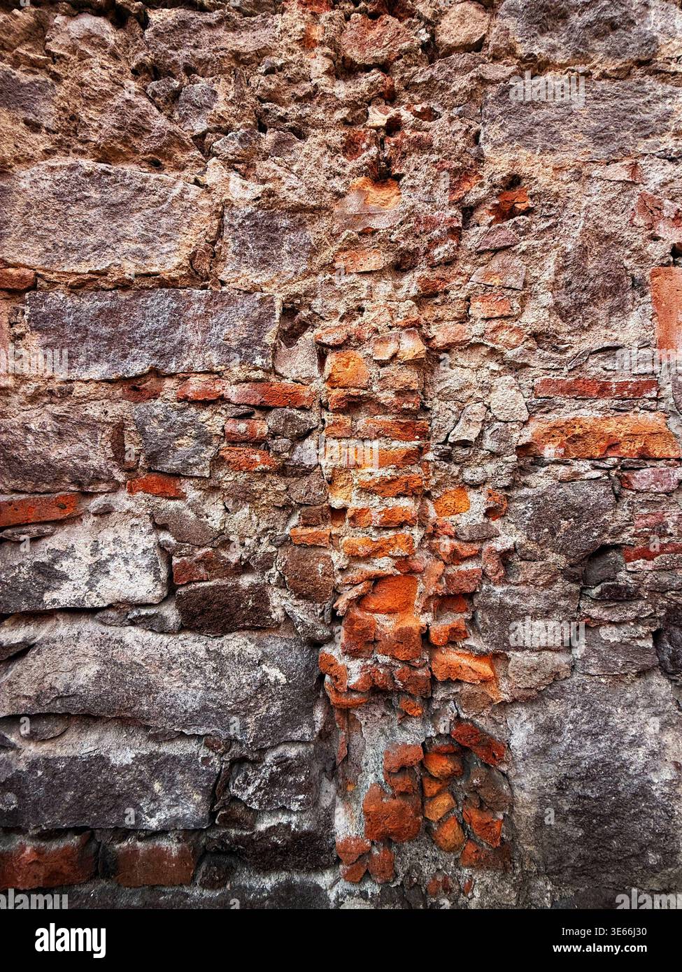 Verwitterte und alte strukturierte Steinmauer mit freiliegenden roten Ziegeln und rauen Mörtelfugen, die historische Architektur zeigen Stockfoto