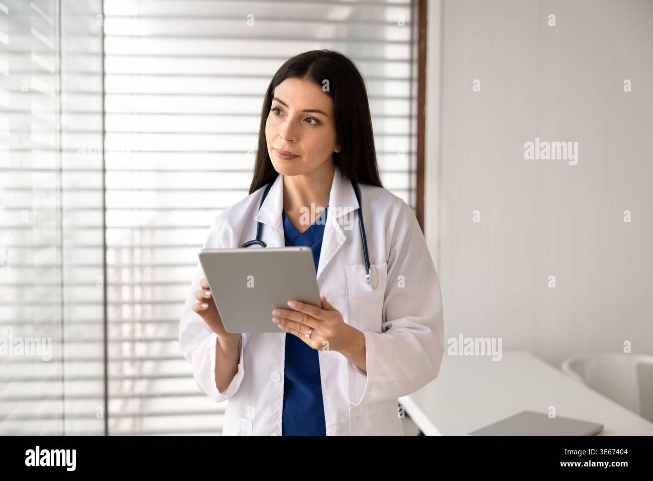 Fokussierter Arzt, der an einem digitalen Tablet arbeitet, steht in der Klinik Stockfoto