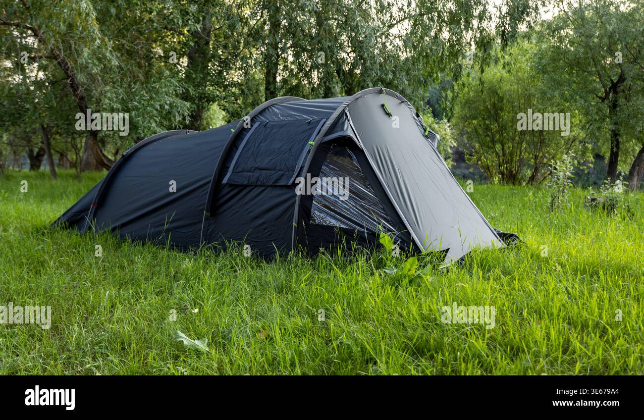 Ein dunkles Touristenzelt im Halbfass-Stil auf grünem Gras in einer Waldlichtung Stockfoto