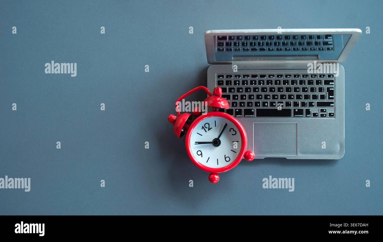 Hochwinkelansicht eines roten Weckers auf einem Miniatur-Laptop, der Termine für die Fernarbeit und Zeitmanagement für digitale Nomaden darstellt. Stockfoto