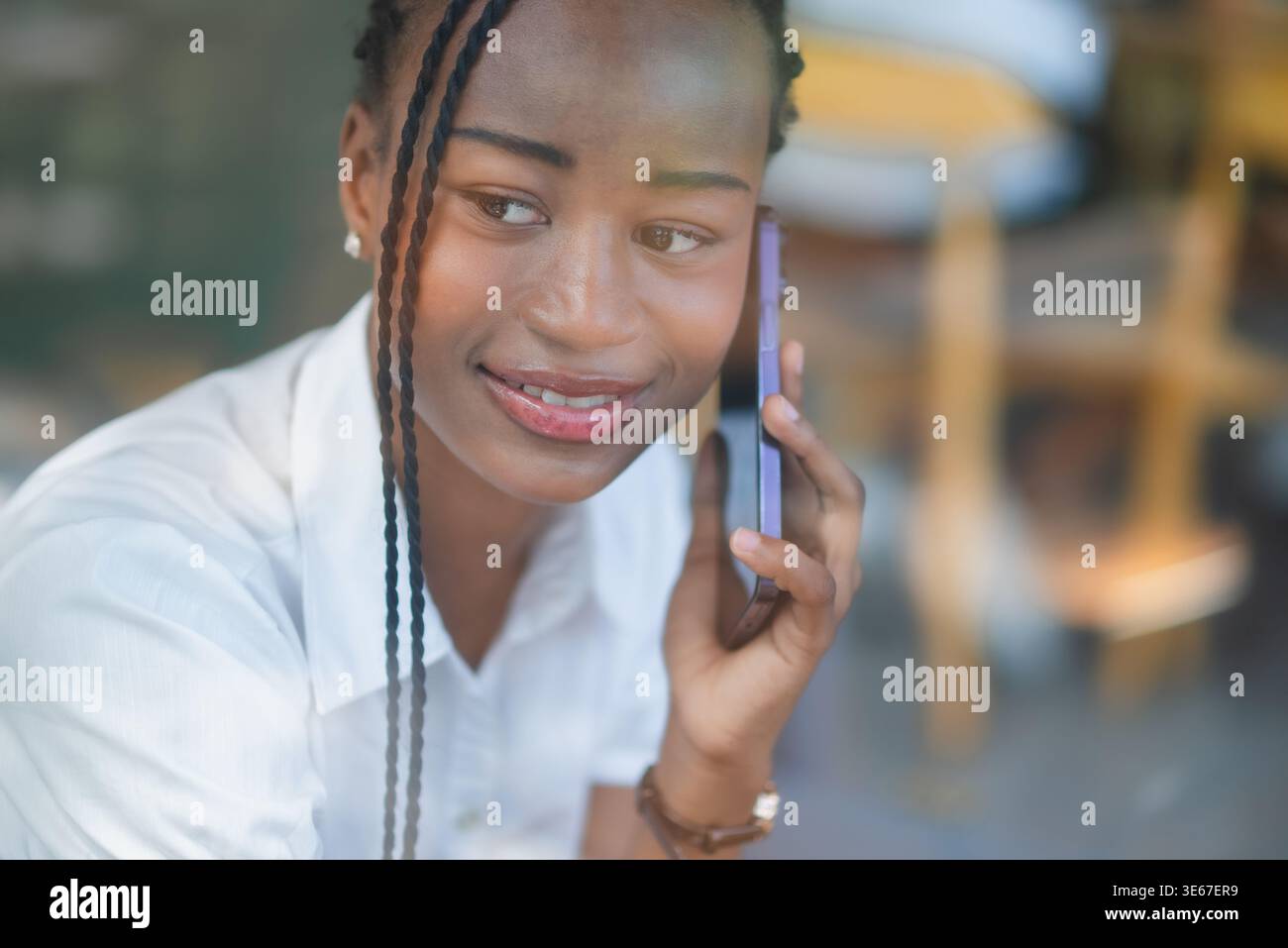 Nahaufnahme eines Porträts einer jungen Schwarzen Frau, die mit einem warmen Lächeln auf dem Smartphone zuhört. Freundliche Unterhaltung, Mobiltechnologie, Kundenservice, persönlich Stockfoto