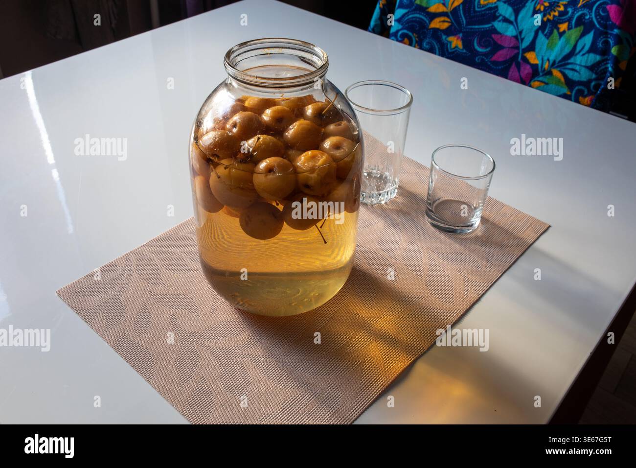 Große Glasdose gefüllt mit hausgemachtem Apfelkompott oder eingelegten Äpfeln auf einem braunen Tischset in einer sonnenbeleuchteten Küche Stockfoto