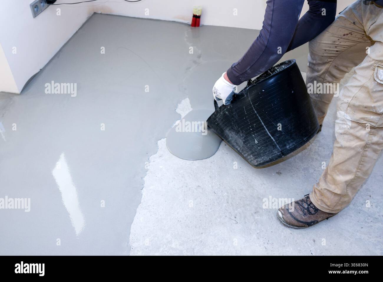 Arbeiter gießen während der Tageszeit für Bauprojekte Zementmischung auf selbstnivellierenden Betonboden in Innenräumen Stockfoto