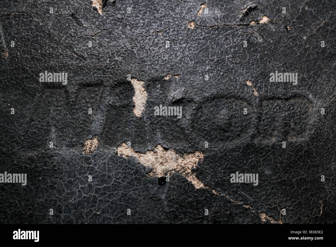 Nahaufnahme von gerissenem, abgetragenem schwarzem Leder mit leicht geprägten Buchstaben und Bereichen, an denen sich die Oberfläche abblätterte, wodurch leichteres Material darunter sichtbar wird Stockfoto