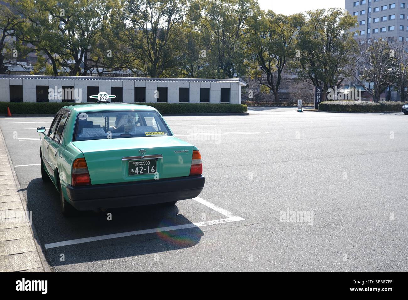 Ein klassisches grünes Toyota Comfort Taxi parkt auf einem großen Stadtparkplatz in Kumamoto, Japan Stockfoto