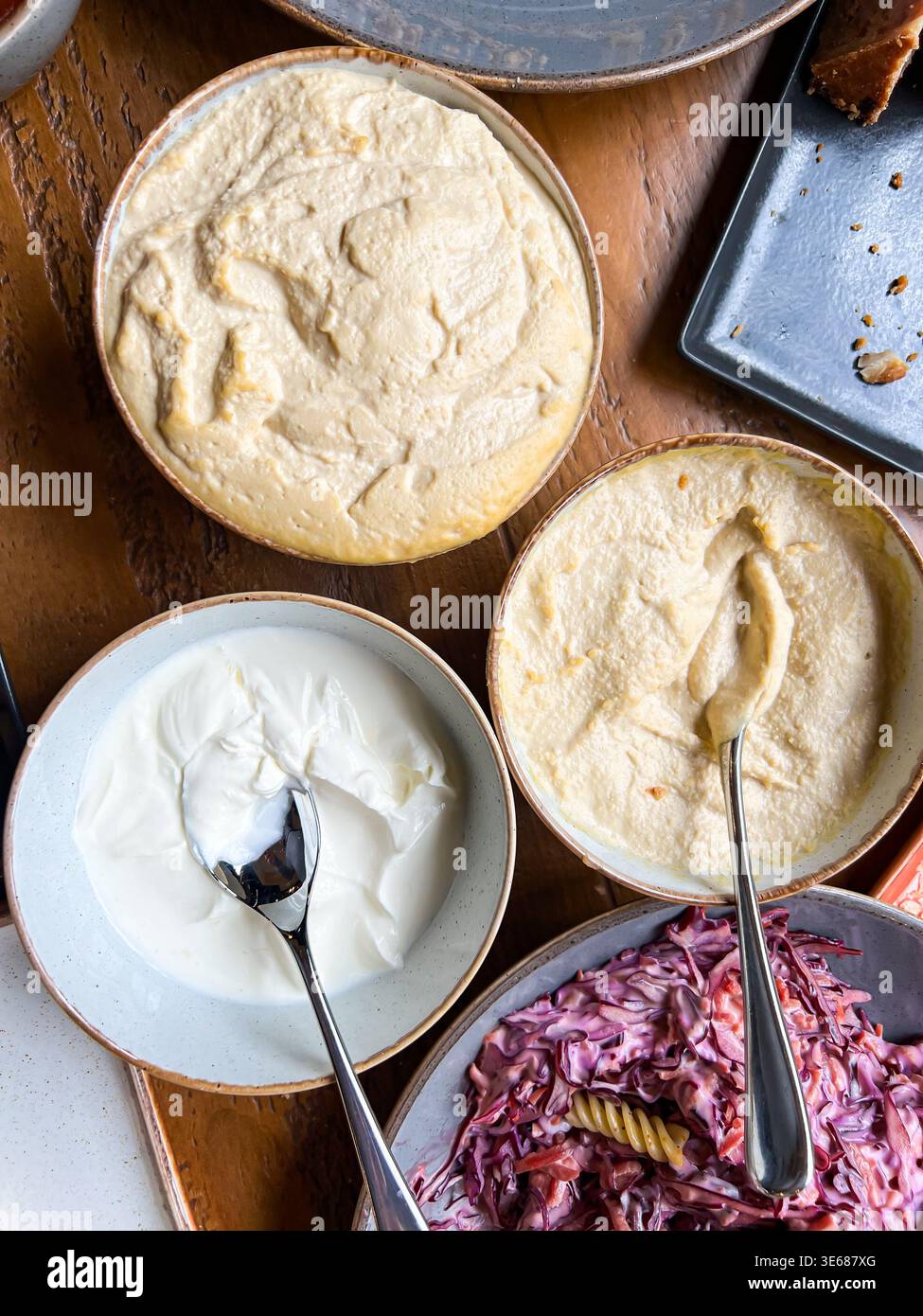 Bei einem Selbstbedienungs-Mittagsbuffet blickt man auf Humus und Mayonnaise in Schüsseln - Smartphone-aufgenommenes Stockfoto