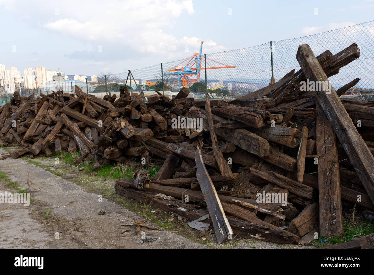 Ein großer, unorganisierter Haufen alter, dunkler, verwitterter Holzbalken oder Eisenbahnschwellen, die auf einem grasbewachsenen Gelände neben einem unbefestigten Weg gestapelt sind. Das Holz zeigt sig Stockfoto