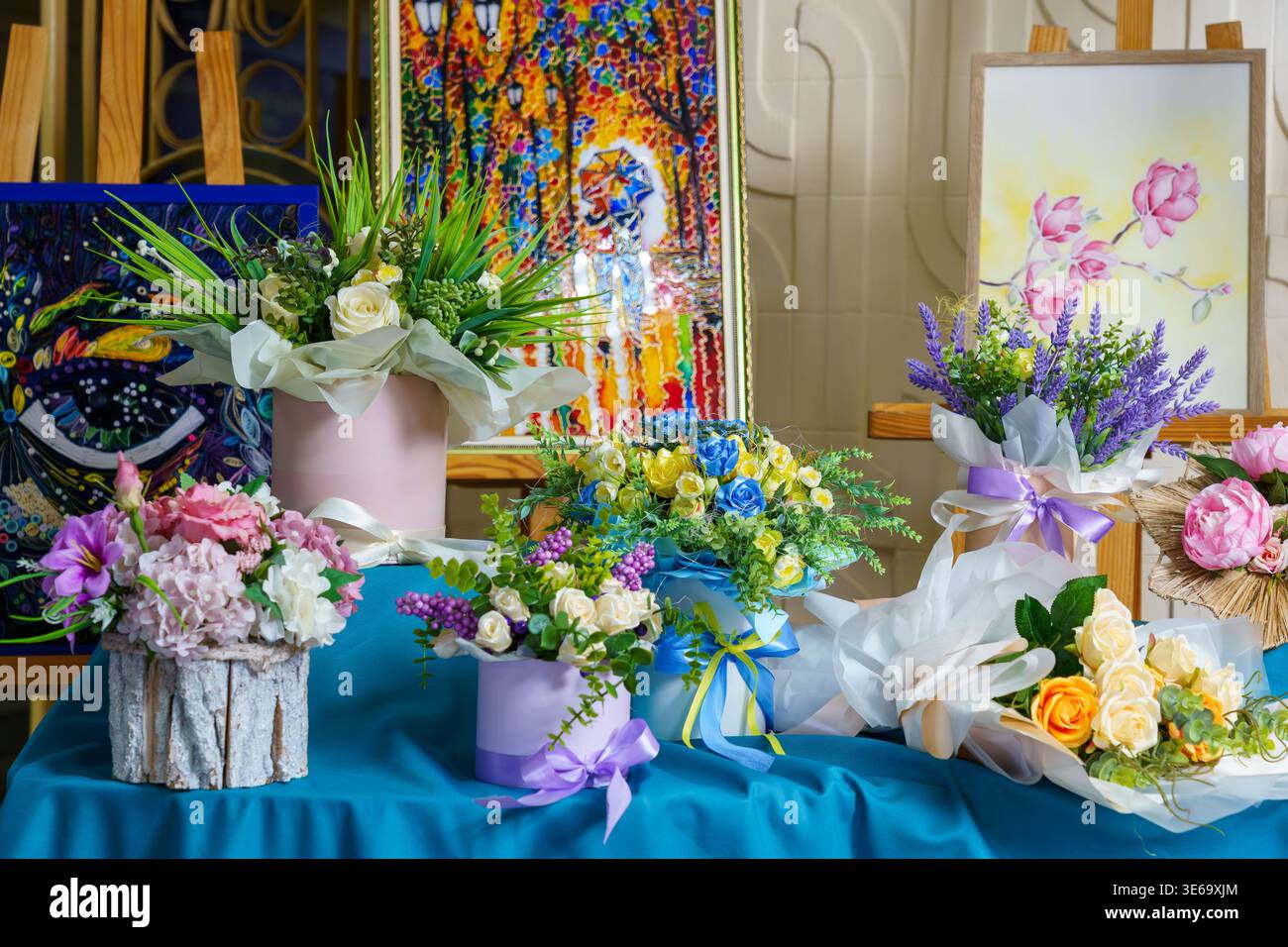 Mehrere Blumenarrangements stehen auf einem blauen Tisch auf einem lokalen Markt. Die Leute kommen vorbei und schauen sich die farbenfrohen Blumen an. Stockfoto