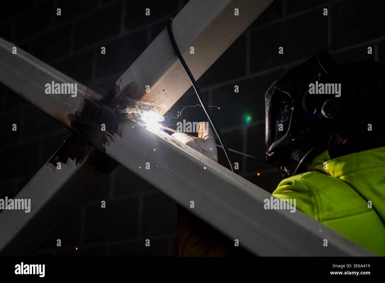 Schweißgerät mit Schutzhelm, das eine Metallrahmenverbindung auf tragenden Stahlträgern verschmilzt, hebt die industrielle Fertigung und Facharbeiter im Bauwesen hervor Stockfoto