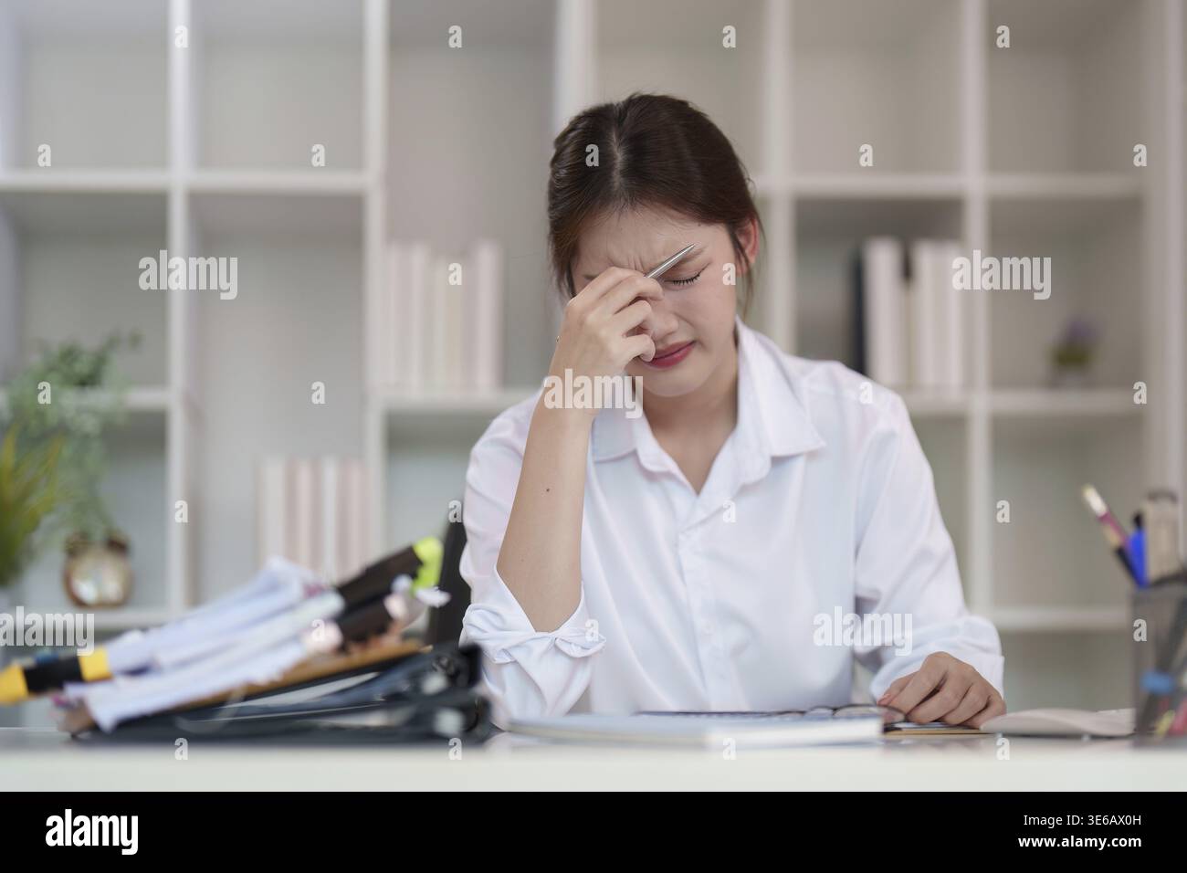 Eine junge Frau sitzt an ihrem Schreibtisch, sichtbar gestresst, während sie Dokumente liest und die Herausforderungen der psychischen Gesundheit in akademischen Umgebungen widerspiegelt Stockfoto