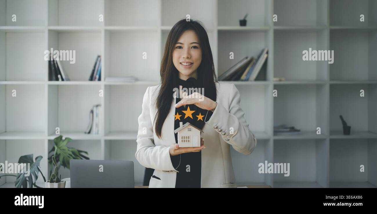 Asiatischer Versicherungsvertreter macht Handsymbol, um das Haus vor einem Unfall zu schützen. Immobilien- und Vertragskonzept Stockfoto