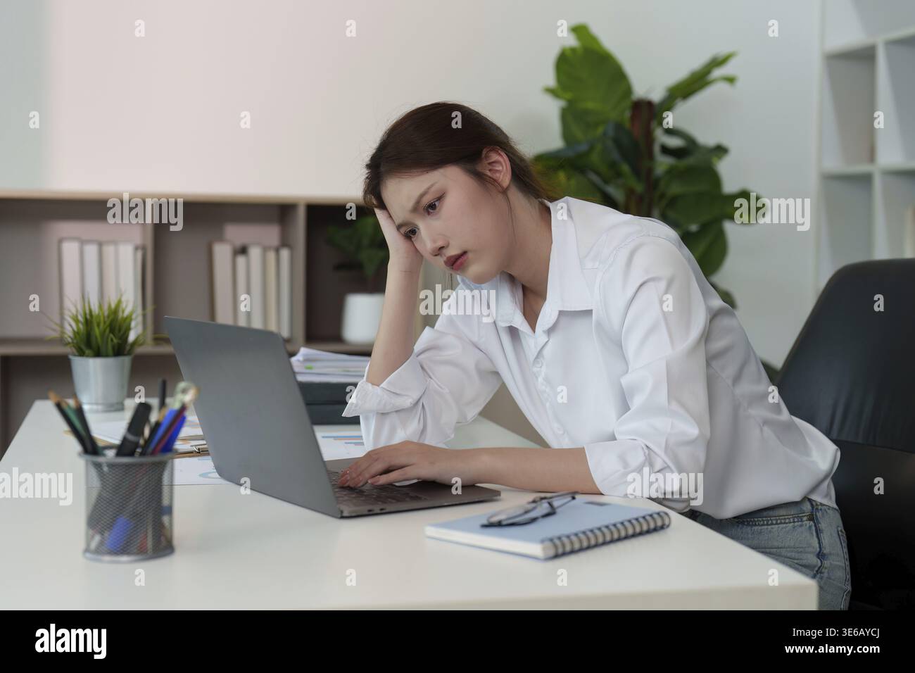 Eine junge Frau schaut aufmerksam auf ihren Laptop und reflektiert die Herausforderungen der Konzentration in einer geschäftigen Arbeitsumgebung Stockfoto
