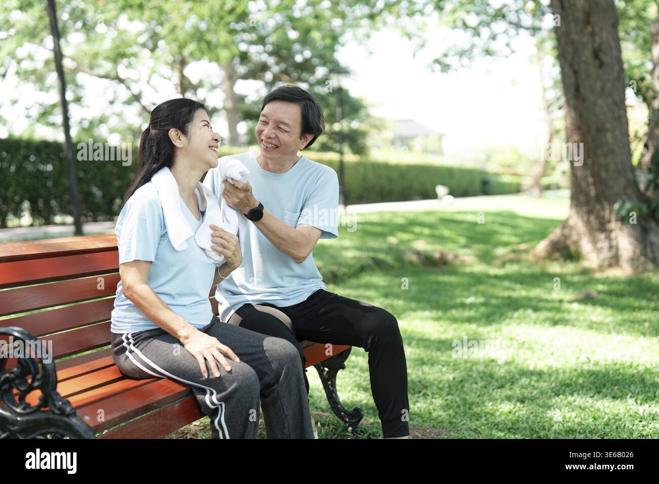 Ein älteres Paar, das auf einer Bank in einem üppigen Park sitzt, einen freudigen Moment teilt und durch Lachen und Zuneigung ihre Bindung pflegt Stockfoto