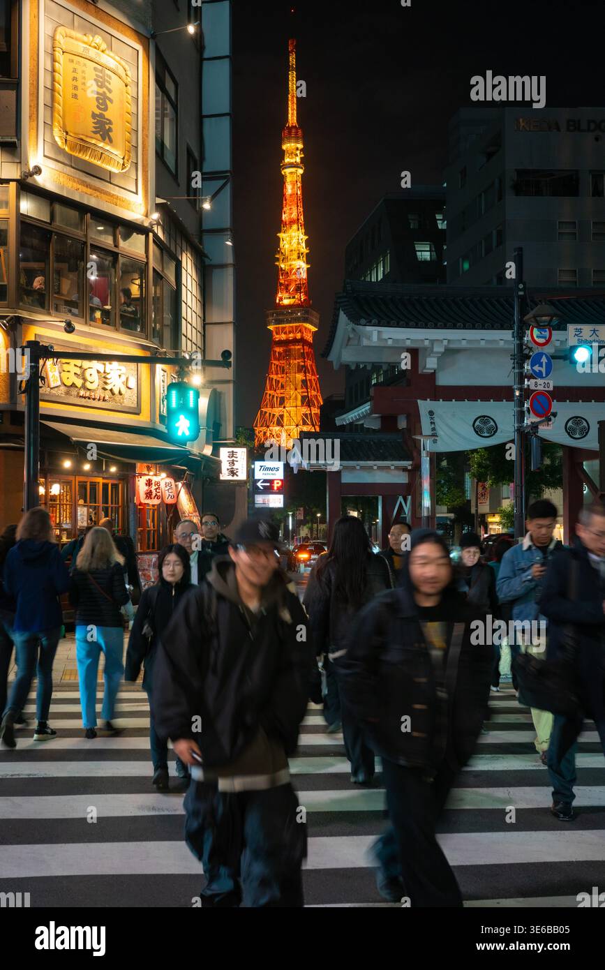 Tokio, Japan - 24. Februar 2026: Der Tokioter Turm ist im Hintergrund beleuchtet und hat eine lebhafte Straßenszene mit Menschen, Fahrzeugen und beleuchteten Ladenschildern. Stockfoto