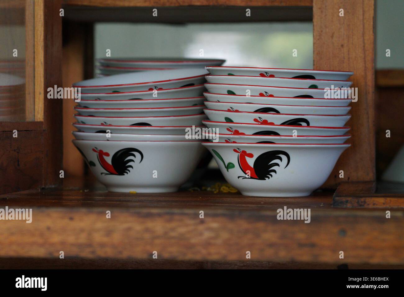 Stapel Keramikschalen mit rotem und schwarzem Hahndesign auf Holzregal. Stockfoto