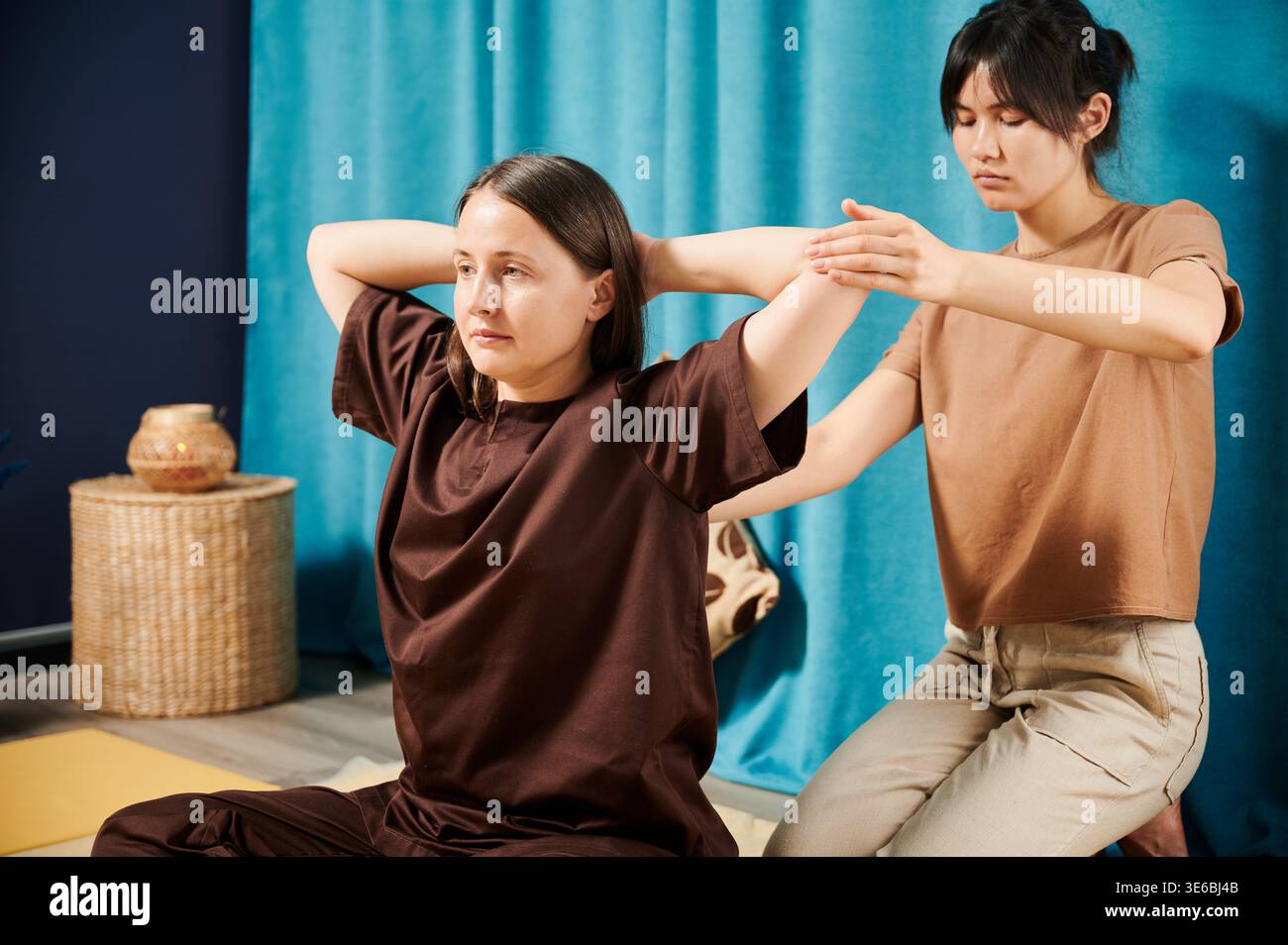 Masseurin, die thai-Yoga-Massage macht. Therapeutin, die traditionelle Massagebehandlung für weibliche Patienten in Innenräumen durchführt. Der Kunde sitzt auf der Matte und genießt eine Handmassage in ruhiger Atmosphäre. Stockfoto