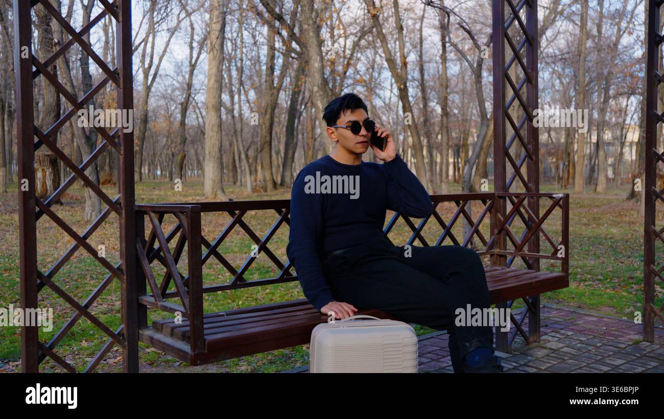 Mann sitzt auf der Bank und spricht telefonisch im Herbstpark Stockfoto