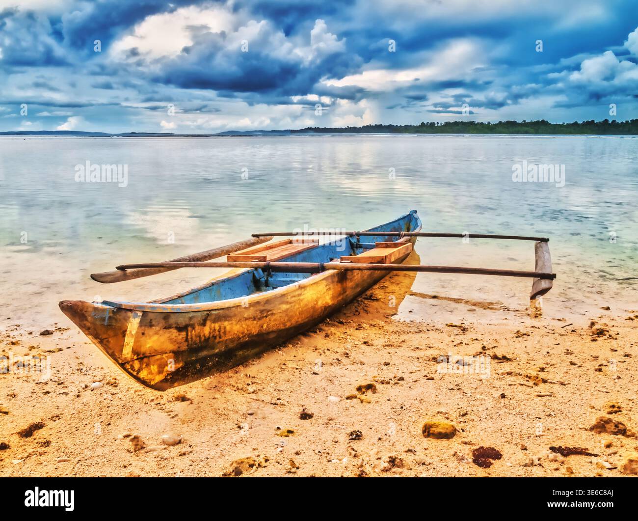 Ein altes hölzernes Auslegerkanu ruht ruhig an einer Sandküste unter bewölktem Himmel Stockfoto