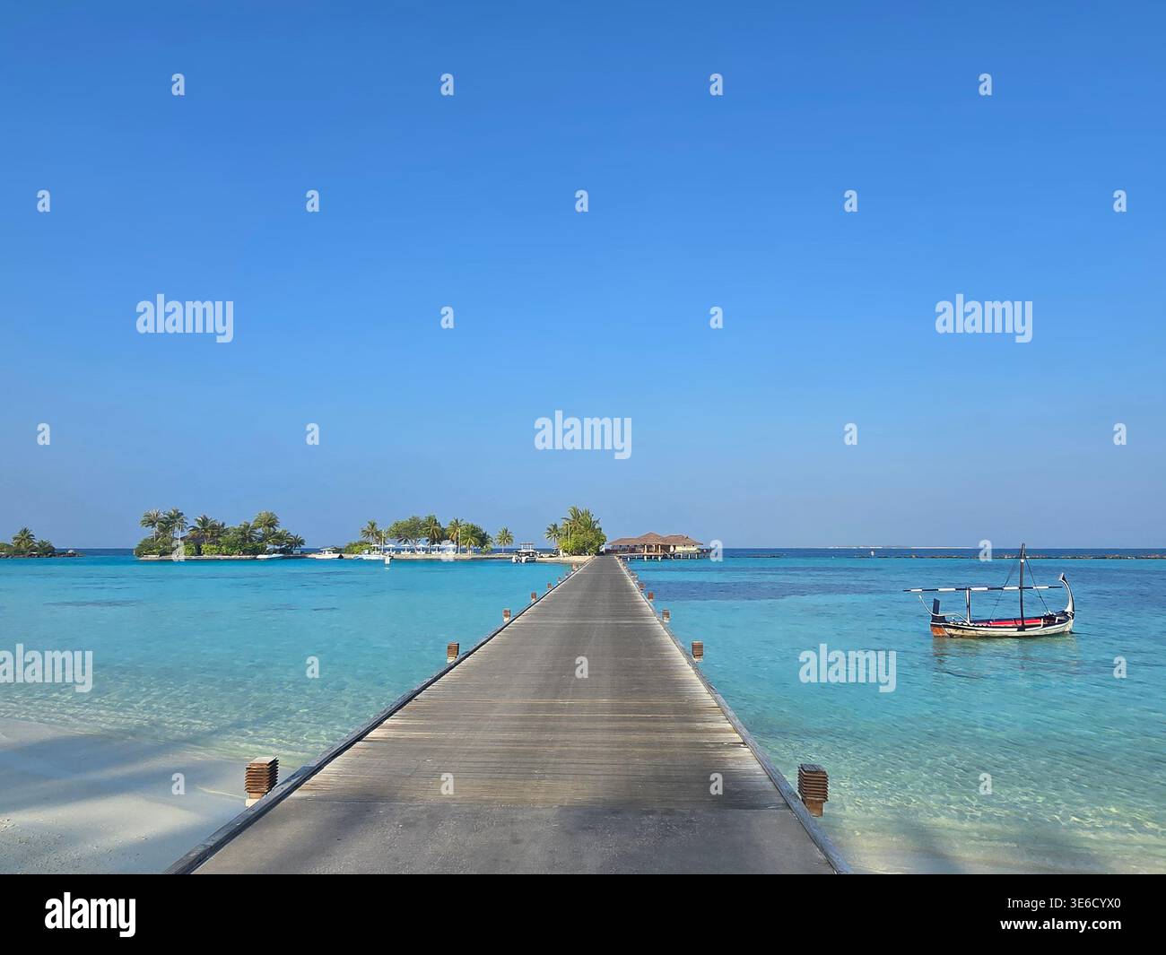 Dieses Hotel verfügt über einen langen Pier, der zu den Überwasser-Villen führt, die an einer türkisfarbenen Lagune liegen. Besucher genießen sonnige Tage am unberührten Strand. Stockfoto