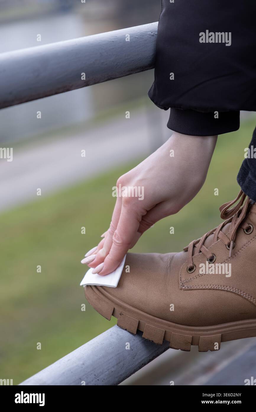 Nahaufnahme einer Person, die auf einem Metallgeländer Schmutz von den Zehen eines robusten braunen Trekkingschuhs abwischt, zeigt die notwendige Pflege der Reiseausrüstung Stockfoto