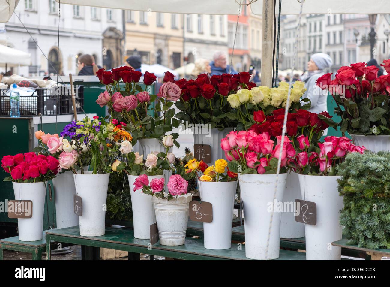 Farbenfrohe, frisch geschnittene Blumen, einschließlich verschiedener Rosen, werden in weißen Eimern mit Preisen ausgestellt, die eine traditionelle Marktszene im Freien und veranschaulichen Stockfoto