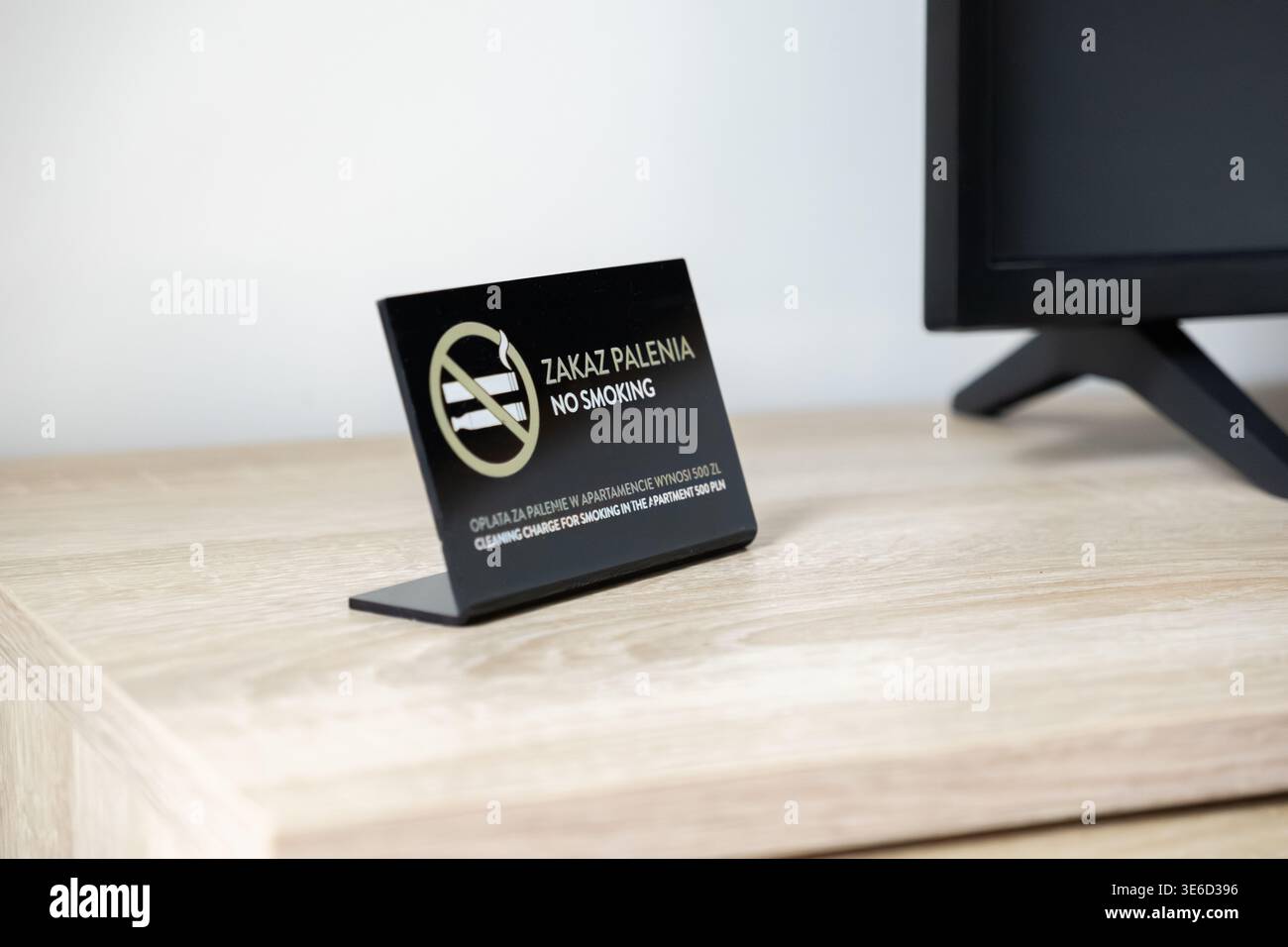 Nahaufnahme eines schwarzen „RAUCHVERBOT“-Richtlinienschildes auf einem hellen Holztisch, der klare Regeln bezüglich Unterkunft, Gesundheit und möglicher Gebühren für vermittelt Stockfoto
