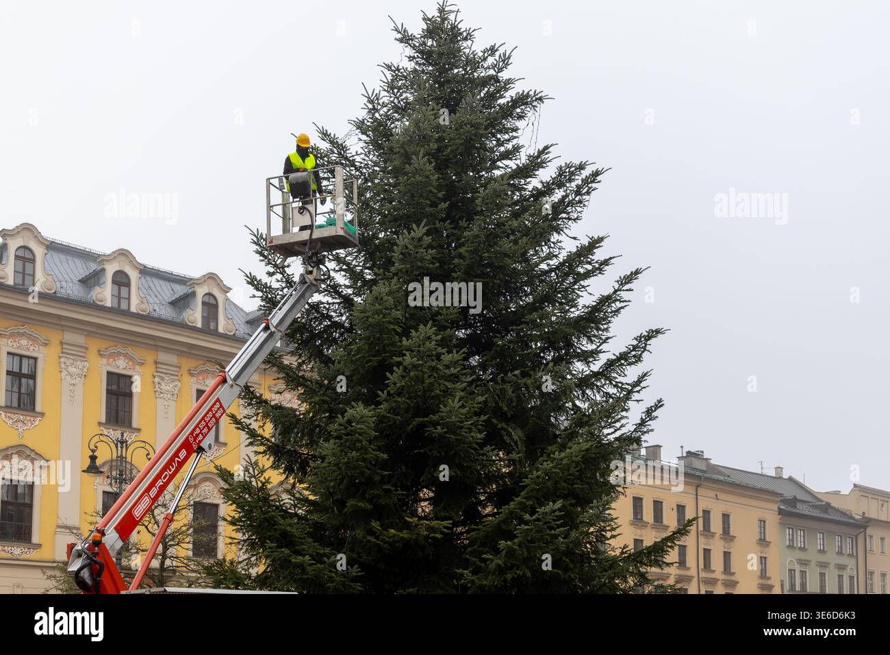 Krakau, Polen - 2. Dezember 2025: Arbeiter in Sicherheitsausrüstung auf einer Luftplattform schmücken großen Weihnachtsbaum im Freien und bereiten sich auf einen festlichen Stadturlaub vor Stockfoto