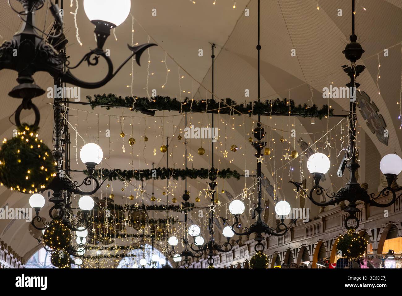 Krakau, Polen - 1. Dezember 2025: Eine wunderschön dekorierte Gewölbehalle mit Lichterketten, goldenen Kugeln und grünen Girlanden schafft eine Stockfoto