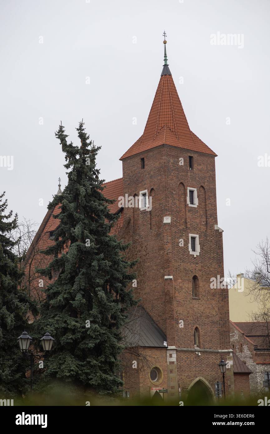 Krakau, Polen - 1. Dezember 2025: Die römisch-katholische Pfarrei des Heiligen Kreuzes steht mit ihrem mächtigen Backsteinturm, dem roten Ziegeldach und dem Kreuz, einer Endur Stockfoto