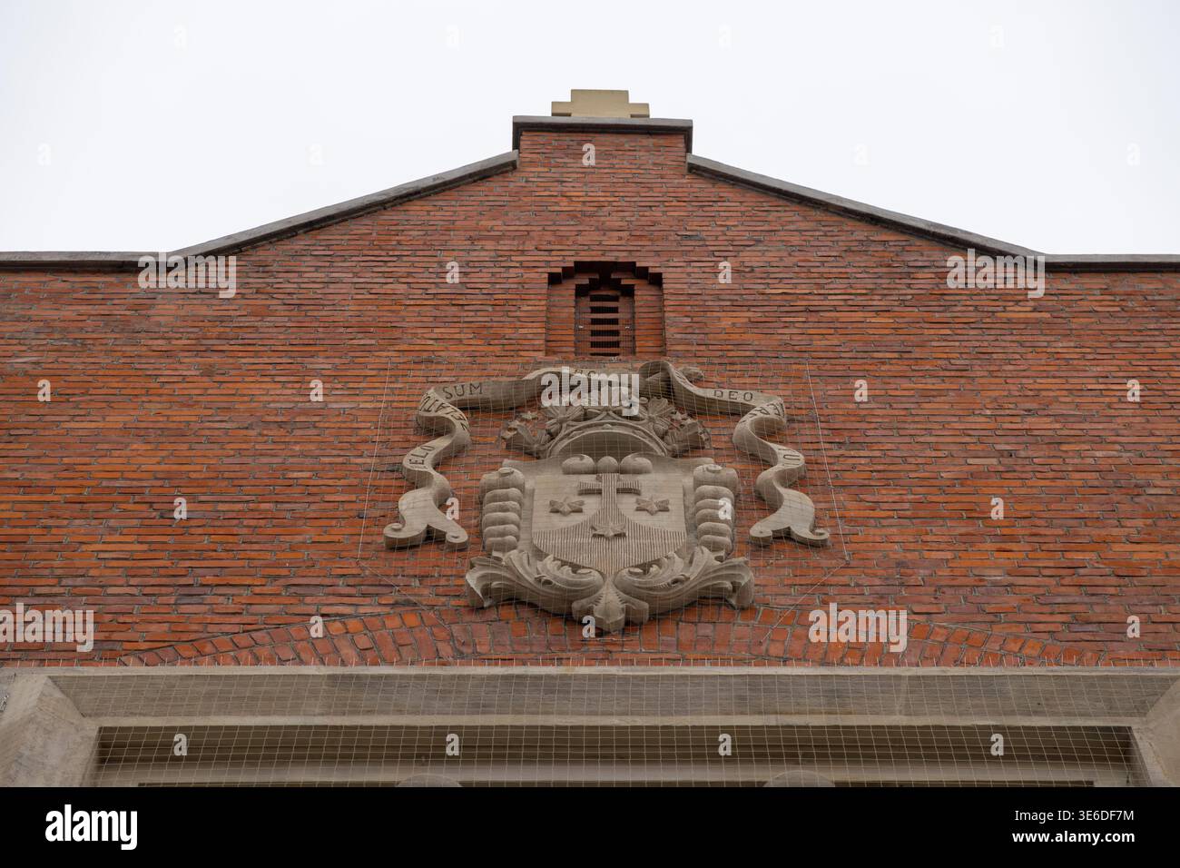 Krakau, Polen - 1. Dezember 2025: Steinwappen mit Kreuz, dekoriert ein altes Gebäude aus rotem Backstein, das historische Architektur und Kultu hervorhebt Stockfoto