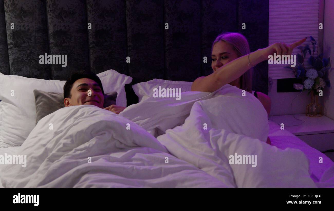 Ein Paar, das mit dem Smartphone spielt und nachts im Bett lacht Stockfoto