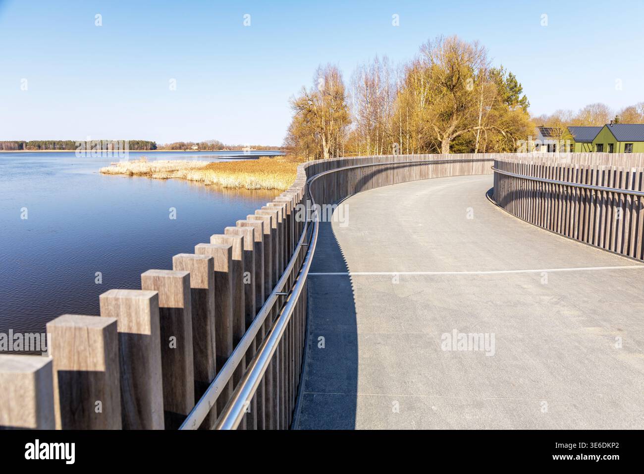 Weitwinkelaufnahme von einer Holzbrücke mit Blick auf einen ruhigen See und einen fernen Wald. Modernes Design, das sich mit der natürlichen Frühlingsumgebung verbindet. Stockfoto