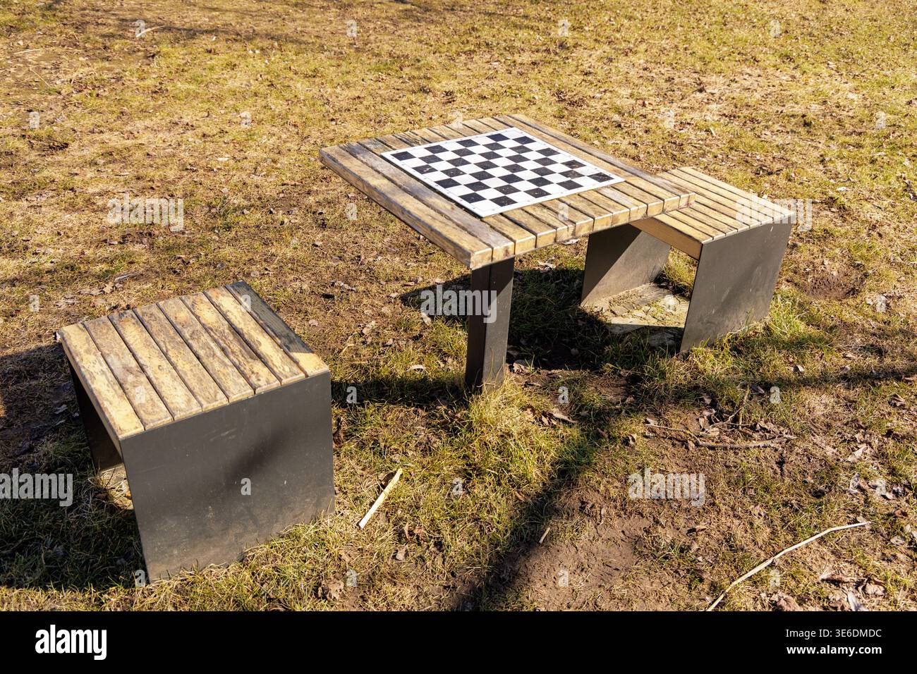 Ein hölzerner Schachtisch und Bänke in einem sonnigen Park im frühen Frühjahr, ideal für Freizeit, Strategie und gemeinschaftliche psychische Gesundheitskonzepte. Stockfoto