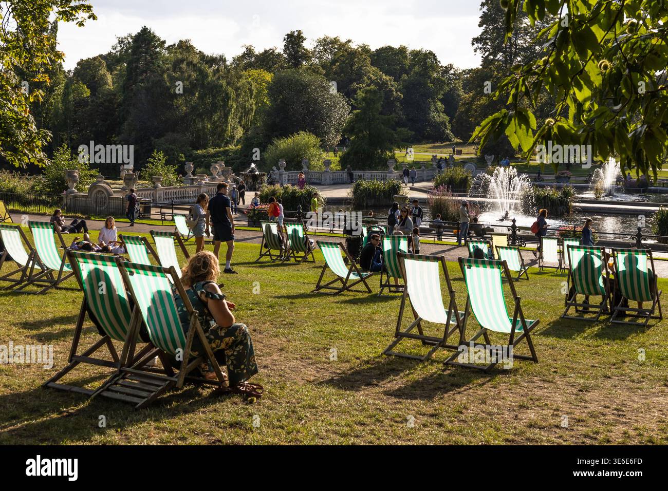Die Leute entspannen sich auf Liegestühlen in einem sonnigen öffentlichen Park Stockfoto